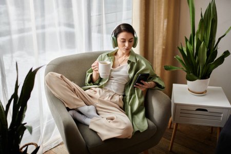 A woman relaxes in an armchair, sipping coffee and listening to music through headphones.