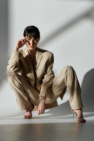 A woman wearing a beige suit poses in a studio setting.