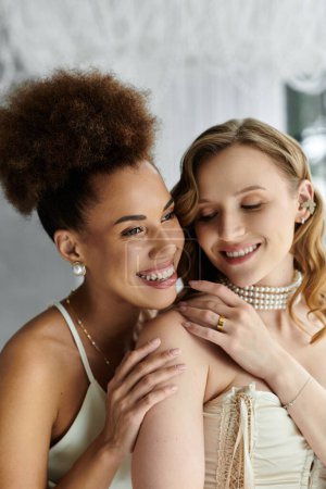 Two brides, one with a curly hair, embrace on their wedding day.