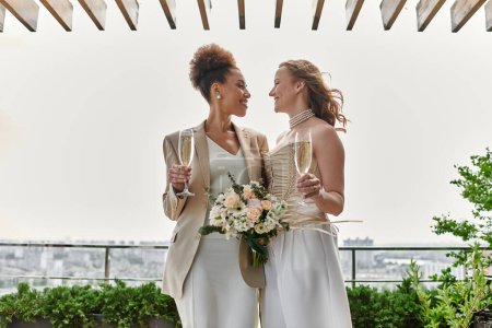 Two brides toast each other with champagne at their rooftop wedding ceremony.