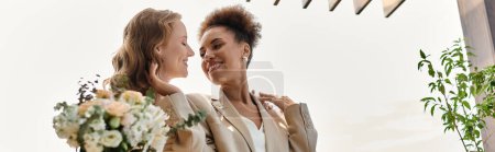 Two women in wedding attire share a loving smile on their wedding day.