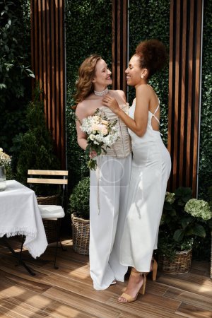 Two brides, dressed in white, smile at each other on their wedding day.