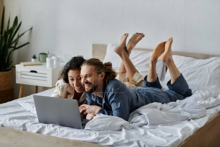 Ein Liebespaar kuschelt im Bett und teilt ein Lachen, während es auf einem Laptop im Internet surft.