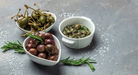 Marinated Green and Kalamata Olives and Capers with fresh rosemary in a small bowl, on light wooden background. Long banner format. top view,