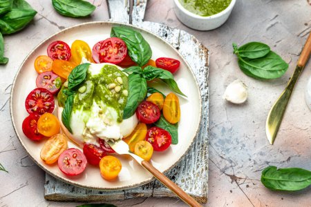 Foto de Salad burrata cheese tomatoes and green pesto. Delicious balanced food concept. superfood concept. Healthy, clean eating. Vegan or gluten free diet. top view. - Imagen libre de derechos