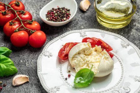 Salat mit cremigem italienischem Burrata-Käse, serviert mit Olivenöl, Basilikumblättern und Kirschtomaten auf weißem Teller auf dunklem Hintergrund. Restaurantmenü, Diät, Kochbuchrezept von oben.