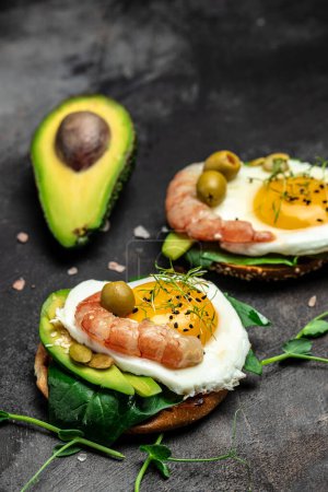 Photo for Breakfast sanwich with wholemeal bread, soft fried egg, spinach, avocado, shrimps on dark background, Ketogenic breakfast. superfood concept. Healthy, clean eating. Top view. - Royalty Free Image