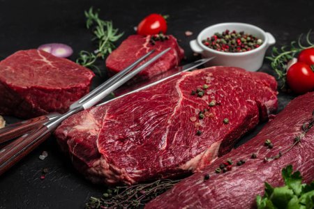 Photo for Variety of fresh raw beef steak with spices for grilling on a dark background. Whole piece of steaks ready to cook. banner, menu, recipe place for text, top view. - Royalty Free Image