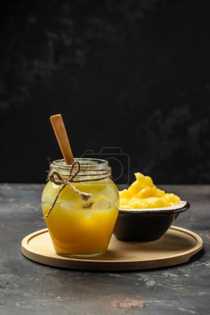 Foto de Puro O Desi Ghee también conocido como mantequilla líquida clarificada en un tazón con cuchara de madera sobre un fondo oscuro. - Imagen libre de derechos
