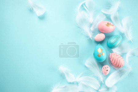 Foto de Decoraciones de Pascua plumas lentejuelas huevos de Pascua de color rosa y blanco sobre fondo azul pastel. Fondo de Pascua. - Imagen libre de derechos