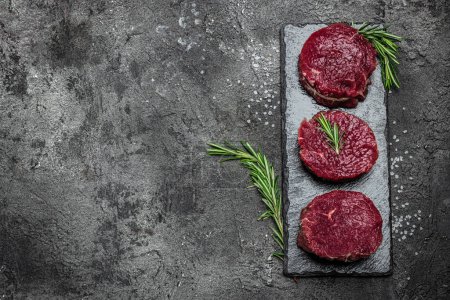 Téléchargez les photos : Viande de bœuf sur fond sombre, Filet entier avec steaks et épices prêt à cuire, - en image libre de droit