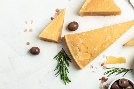 Parmesan cheese on a wooden board, Hard cheese, olives, rosemary and metal grater on a light background. place for text, top view.