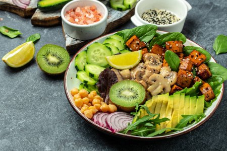 Téléchargez les photos : Teriyaki baked tofu with avocado, chickpeas, cucumber and mushrooms. buddha bowl. Vegan lunch salad. Food recipe background. Close up. - en image libre de droit