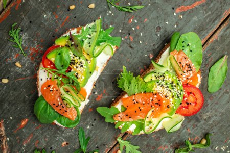 sandwich with cream cheese, salmon, avocado, cucumber, tomato and greens on a dark background. Keto breakfast or brunch. banner, menu, recipe place for text, top view.