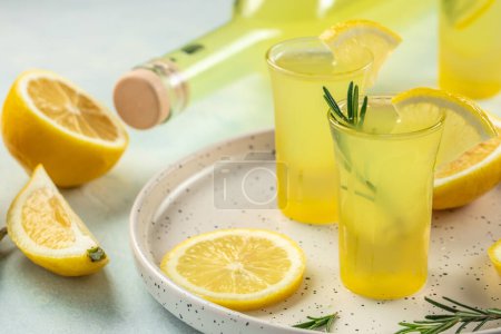 Photo for Italian traditional liqueur limoncello with rosemary and lemons on a light background. place for text. - Royalty Free Image