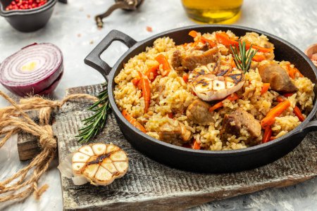 Téléchargez les photos : Pilaf alimentaire ouzbek dans une casserole en fonte. bannière, menu, lieu de recette pour le texte. - en image libre de droit