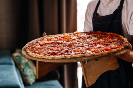 Photo for The waiter holds a tray of large pizzas in a restaurant. Hot big pepperoni pizza tasty pizza composition with melting cheese bacon tomatoes ham paprika. - Royalty Free Image