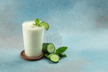 Téléchargez les photos : Yogourt maison Ayran boisson avec du concombre frais sur un fond bleu, manger propre pour perdre du poids. place pour le texte. - en image libre de droit