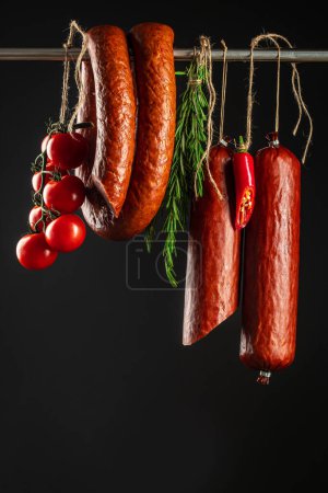 Téléchargez les photos : Saucisse de salami fumée traditionnelle au romarin sur fond sombre, - en image libre de droit