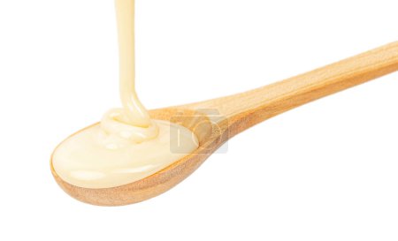 Téléchargez les photos : Verser du lait condensé dans une cuillère en bois isolée sur du blanc. - en image libre de droit
