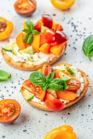 Open sandwiches with cream cheese, peaches, tomatoes and green basil leaves on white background. top view.