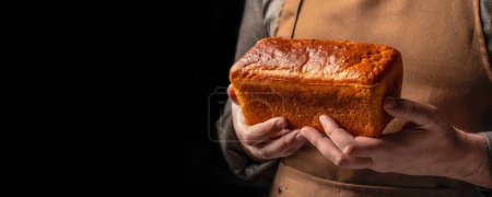 Man holding Small brown bread in his hands. bakery products on a dark background. Long banner format.