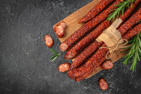 Long meat sausages. Kabanosy sausages pork on a board with fresh herbs on a dark background. top view. copy space for text.