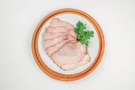 Sliced smoked ham with herbs and aromatic spices on plate.