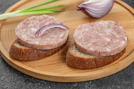 Headcheese sandwich with onions on a wooden board,