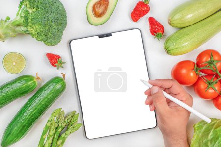 Männliche Hand mit einer Vielzahl von frischem Gemüse, die an einem digitalen Tablet arbeitet. gesunde biologische Produkte. Detox und sauberes Ernährungskonzept. Digitale Lebensmittel.