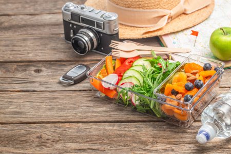 nourriture voyage déjeuner boîte avec fruits, légumes. carte, caméra film vintage, chapeau de plage en osier sur fond de table en bois, vue sur le dessus