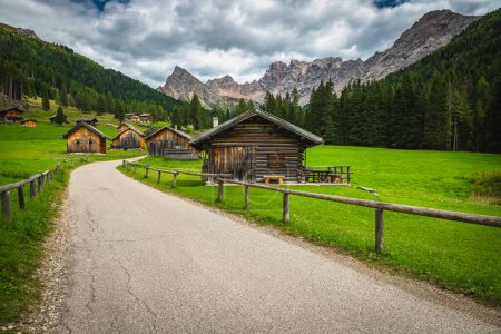 Picturesque San Nicolo valley view with gardens, wooden log huts and admirable high mountains in background, Dolomites, Italy, Europe