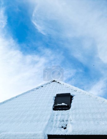 Téléchargez les photos : Fenêtre de toit ouverte de style velux avec des tuiles noires recouvertes de neige en hiver - en image libre de droit