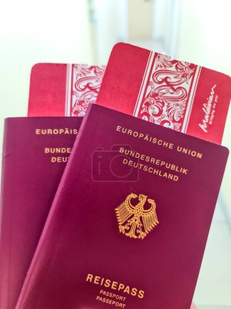 Foto de Una mano sostiene dos pasaportes alemanes frente a un fondo de viaje suave con tarjetas de embarque a las Maldivas - Imagen libre de derechos