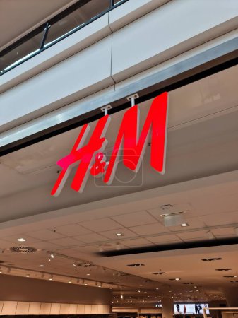 Foto de Kiel, Alemania - 01. Abril 2024: Un gran logotipo rojo H y M de la marca Hennes y Mauritz por encima de la entrada de una tienda - Imagen libre de derechos
