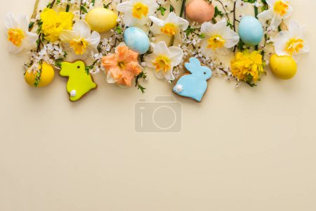 Fond festif avec des fleurs de printemps et des ?ufs de couleur naturelle et des lapins de Pâques, des jonquilles blanches et des branches de fleurs de cerisier sur un fond jaune pastel