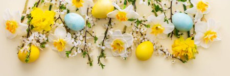 Festive banner with spring flowers and Easter eggs, white daffodils and cherry blossom branches on a yellow pastel background