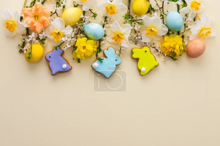 Festive background with spring flowers and naturally colored eggs and Easter bunnies, white daffodils and cherry blossom branches on a yellow pastel background