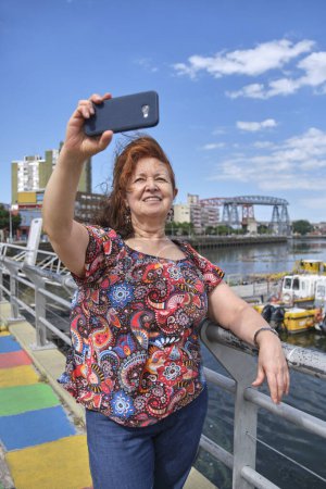 Téléchargez les photos : Touriste féminine faisant un autoportrait avec son smartphone dans le quartier touristique de La Boca, à Buenos Aires, Argentine, par une journée d'été ensoleillée. - en image libre de droit