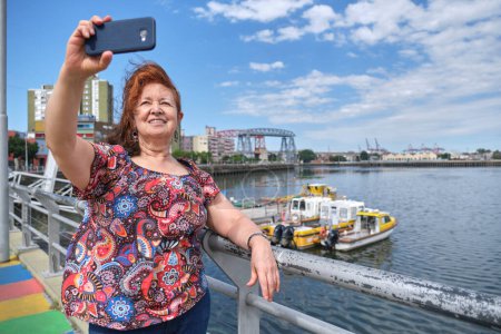 Téléchargez les photos : Femme latine mature prenant un selfie avec son smartphone dans le quartier touristique de La Boca, à Buenos Aires, en Argentine, par une journée d'été ensoleillée. - en image libre de droit