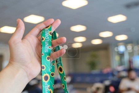 Unerkennbare Person mit einem Schlüsselband aus Sonnenblumen, Symbol für Menschen mit unsichtbaren oder versteckten Behinderungen, in einem Reisekontext, einem Wartezimmer auf einem Flughafen.