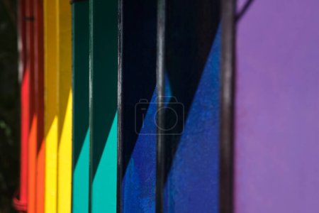 Photo for Rainbow colored fence under hard light, parallel vertical lines, and diagonals; light and shadow colorful areas. - Royalty Free Image