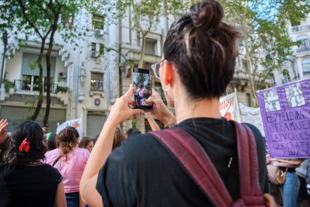 Téléchargez les photos : Buenos Aires, Argentine ; 8 mars 2023 : grève féministe internationale. Jeune femme prenant des photos et des vidéos pendant que des groupes de femmes défilent et chantent des slogans. - en image libre de droit