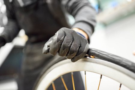 Photo for Unrecognizable bicycle mechanic using protective gloves removing an airless tire from a bike wheel at a repair shop. Selective focus composition with copy space. - Royalty Free Image