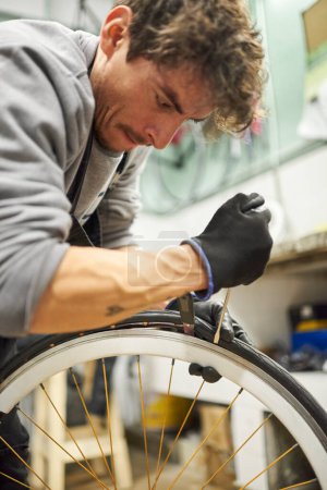Photo for Hispanic bicycle mechanic using protective gloves removing an airless tire from a bike wheel at a repair shop. Selective focus composition with copy space. - Royalty Free Image