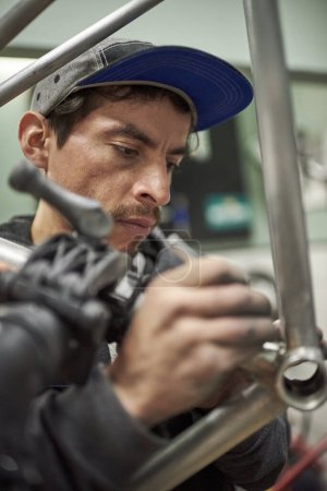 Foto de Hombre hispano eliminando residuos de pintura de un cuadro de bicicleta como parte del proceso de renovación de una bicicleta realizado en su taller. - Imagen libre de derechos