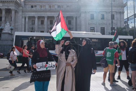 Foto de Buenos Aires, Argentina, 16 de febrero de 2024: Mujeres levantando una bandera palestina, personas reunidas frente al Congreso Nacional en solidaridad con Palestina y contra el ataque genocida de Israel. - Imagen libre de derechos