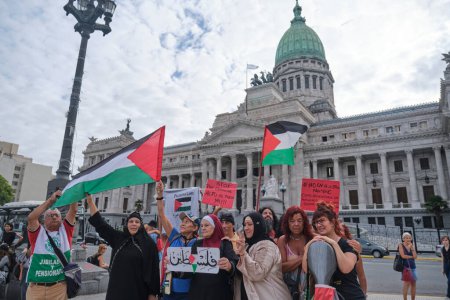 Foto de Buenos Aires, Argentina, 16 de febrero de 2024: Mujeres levantando banderas palestinas y carteles pacifistas, personas reunidas frente al Congreso en solidaridad con Palestina y contra el ataque genocida de Israel. - Imagen libre de derechos