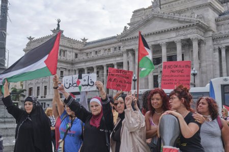 Foto de Buenos Aires, Argentina, 16 de febrero de 2024: Mujeres levantando banderas palestinas y carteles pacifistas, personas reunidas frente al Congreso en solidaridad con Palestina y contra el ataque genocida de Israel. - Imagen libre de derechos