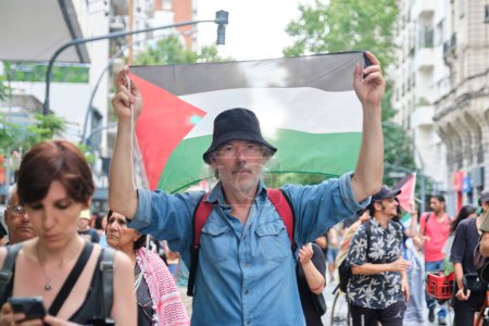 Foto de Buenos Aires, Argentina, 16 de febrero de 2024: Hombre levantando una bandera palestina, marchando en apoyo y solidaridad con Palestina y contra el ataque genocida de Israel. - Imagen libre de derechos